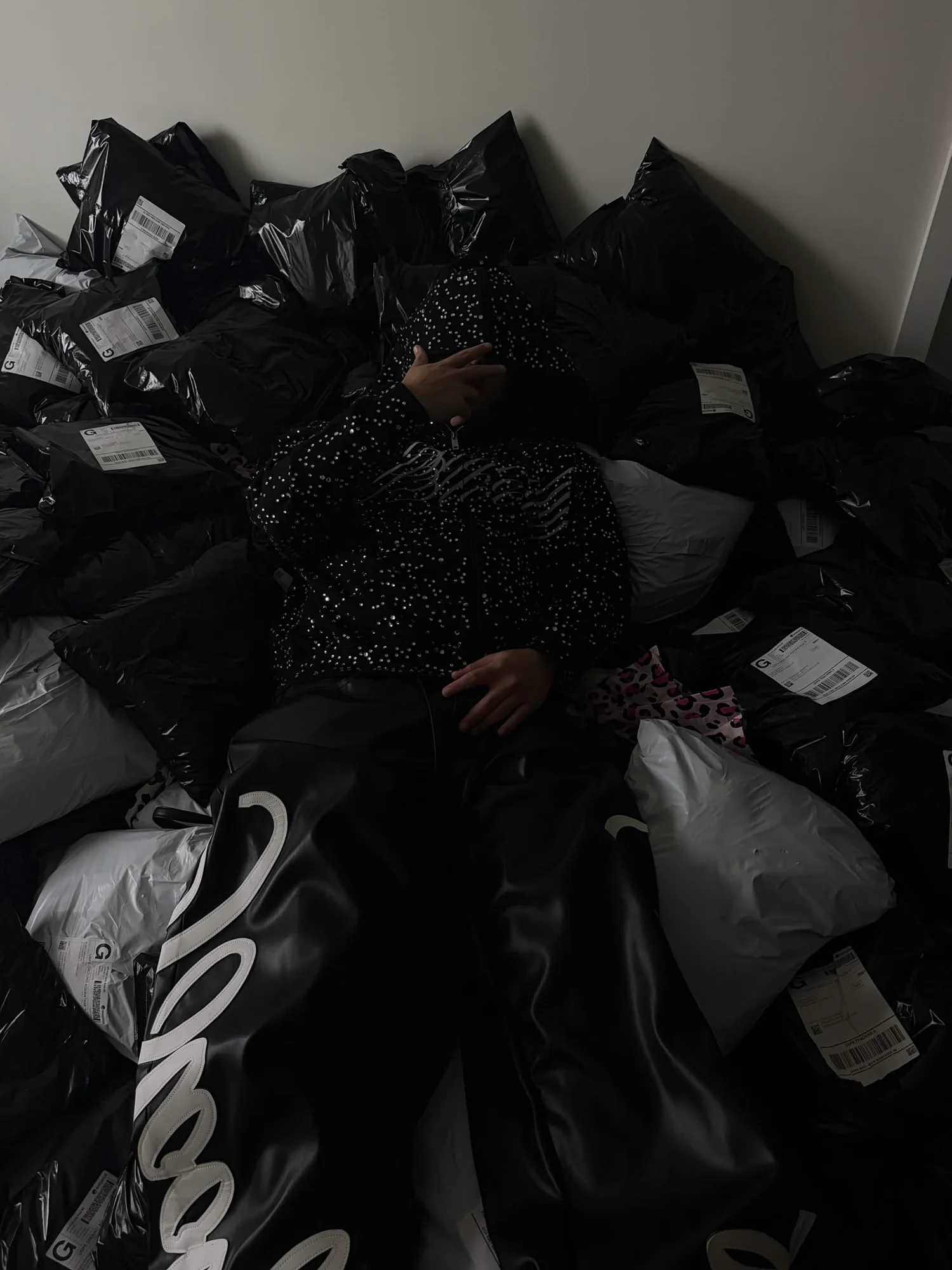 Jojo lying back on a floor covered in packed black and white poly mailer orders, ready to ship out after a drop.